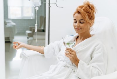 Portrait view of the charming woman in white bathrobe sitting in armchair and receiving IV infusion